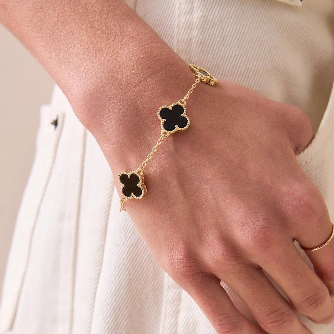 Hand wearing a gold bracelet with black clover-shaped charms on a white background